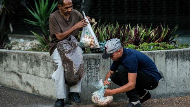 Dos hombres buscan comida en bolsas de basura en Caracas.